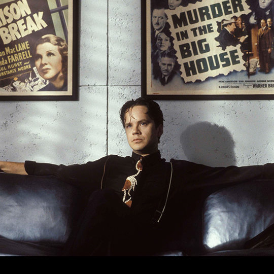 A single person sitting on a black leather couch with arms outstretched with two retro film posters framed on the wall above them